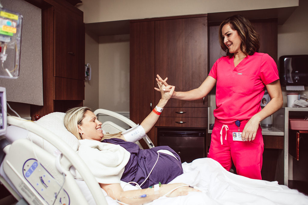 Położna i kobieta rodząca splatają ręce w geście wsparcia.