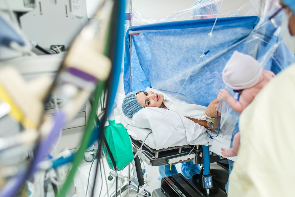 Kobieta patrzy na noworodka leżąc na łóżku szpitalnym.