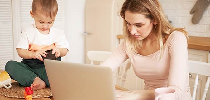 Kobieta pracująca na komputerze obok bawi się dziecko